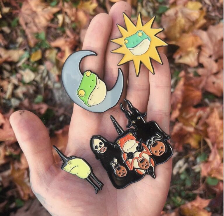 A hand holding colorful sun, moon and witch pins by Bill Crisafi