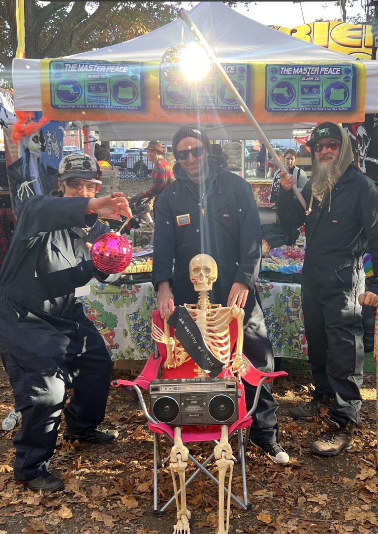 The Master Peace booth with team members, colorful displays, and a skeleton decoration