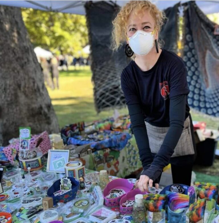 A maker at the Master Peace With Love booth beside colorful handmade goods