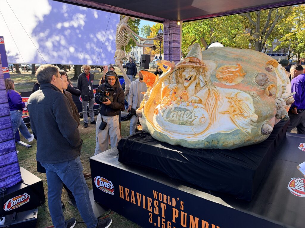 The 3,156-pound Raising Cane's world-record jack-o'-lantern, carved with a witch stirring a cauldron, on display under a tent on Salem Common.